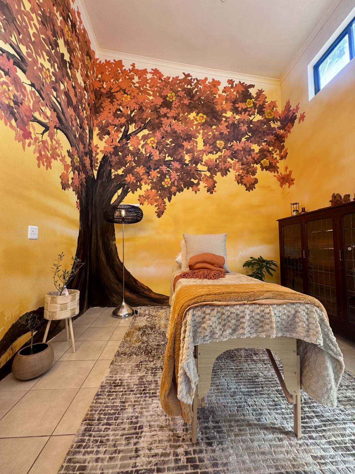 The Roots and Radiance treatment room with its Tree of Life mural and treatment bed