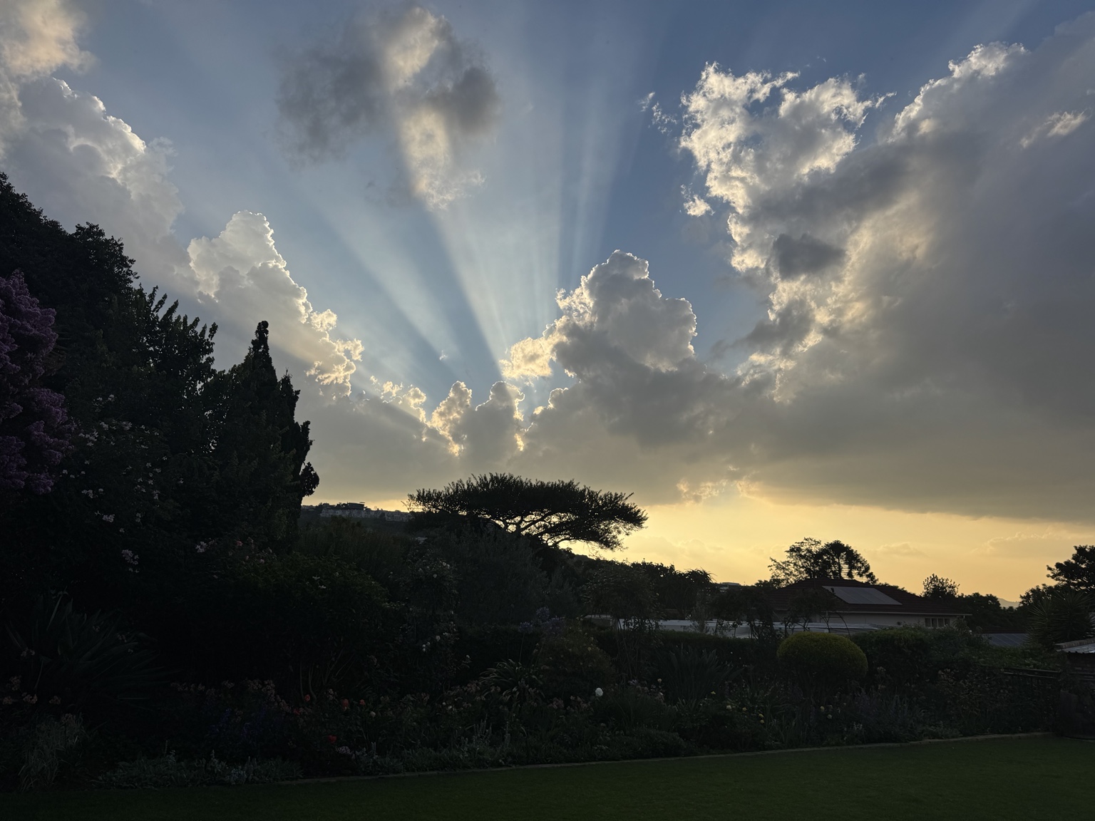 Sun rays streaming through clouds above the garden at sunset